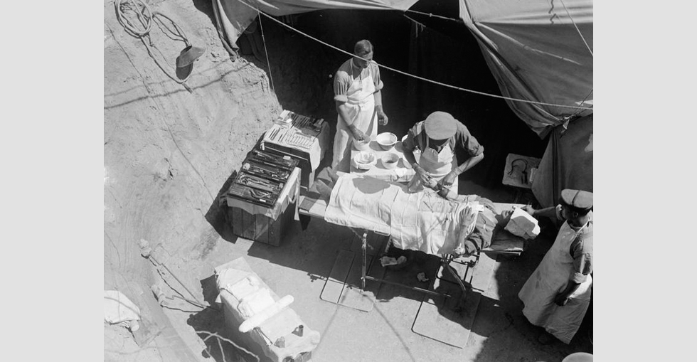 A surgeon is removing a bullet from the patients right arm in the operation dugout of the Field Ambulance of the 42nd (East Lancashire) Division.